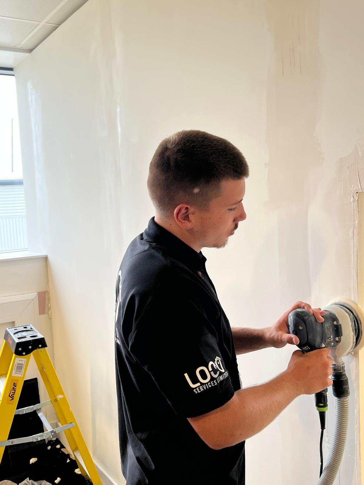 LOCO team member sanding a wall in preparation for finishing
